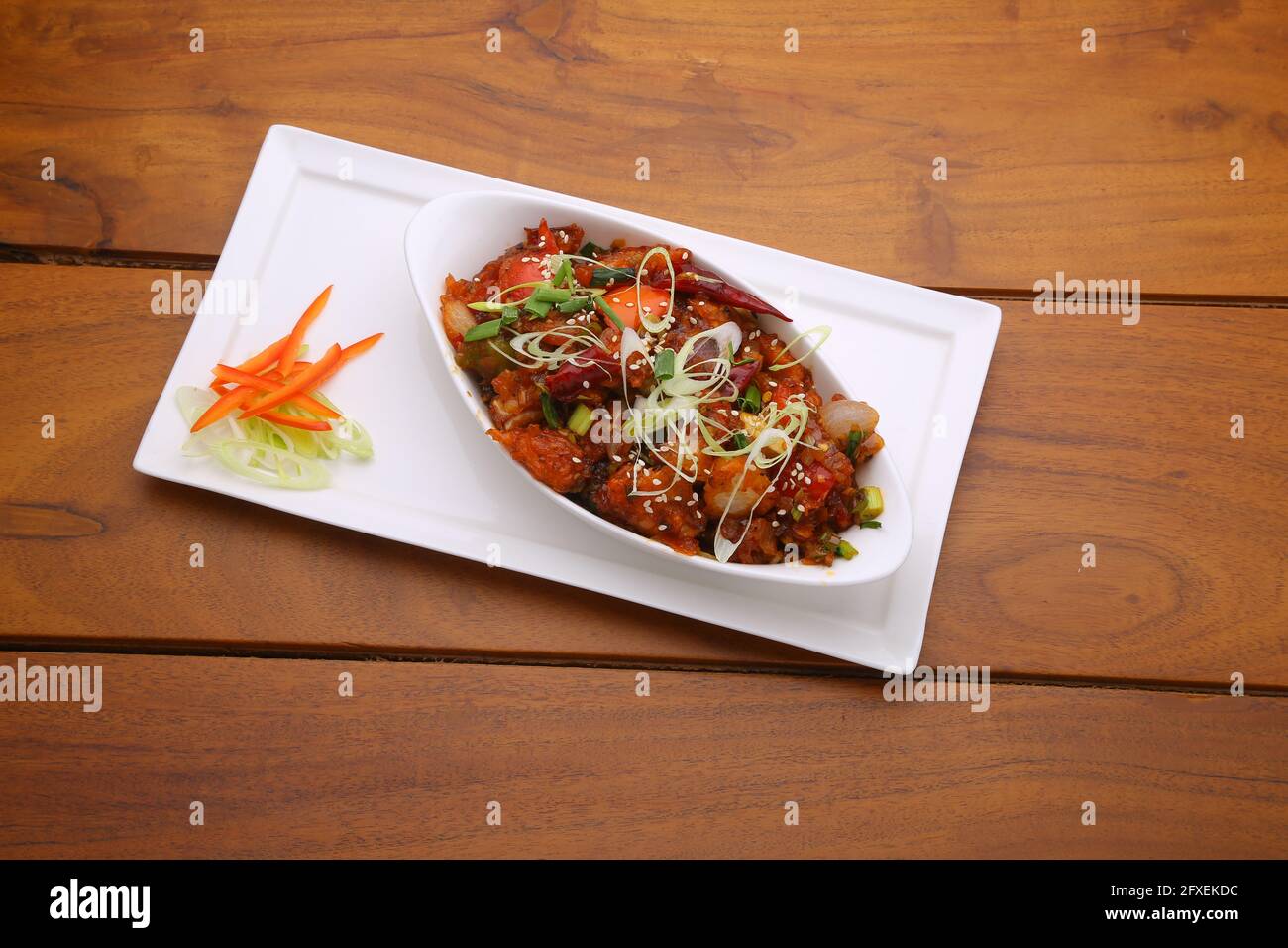 Chili poulet sec, bien garni et disposé dans une forme ovale bol sur une assiette de service blanche à texture bois Banque D'Images