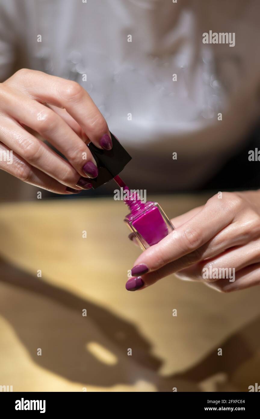 Gros plan de mains de femmes tenant une bouteille de vernis à ongles Tyrian violet Banque D'Images