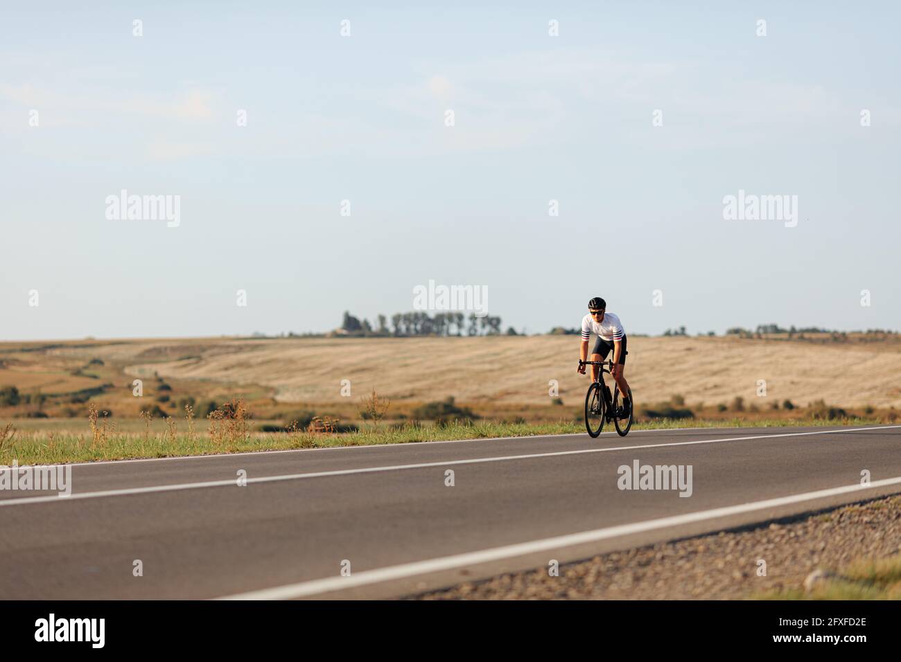 Jeune homme actif qui fait du vélo sur la route pendant la journée ensoleillée Banque D'Images