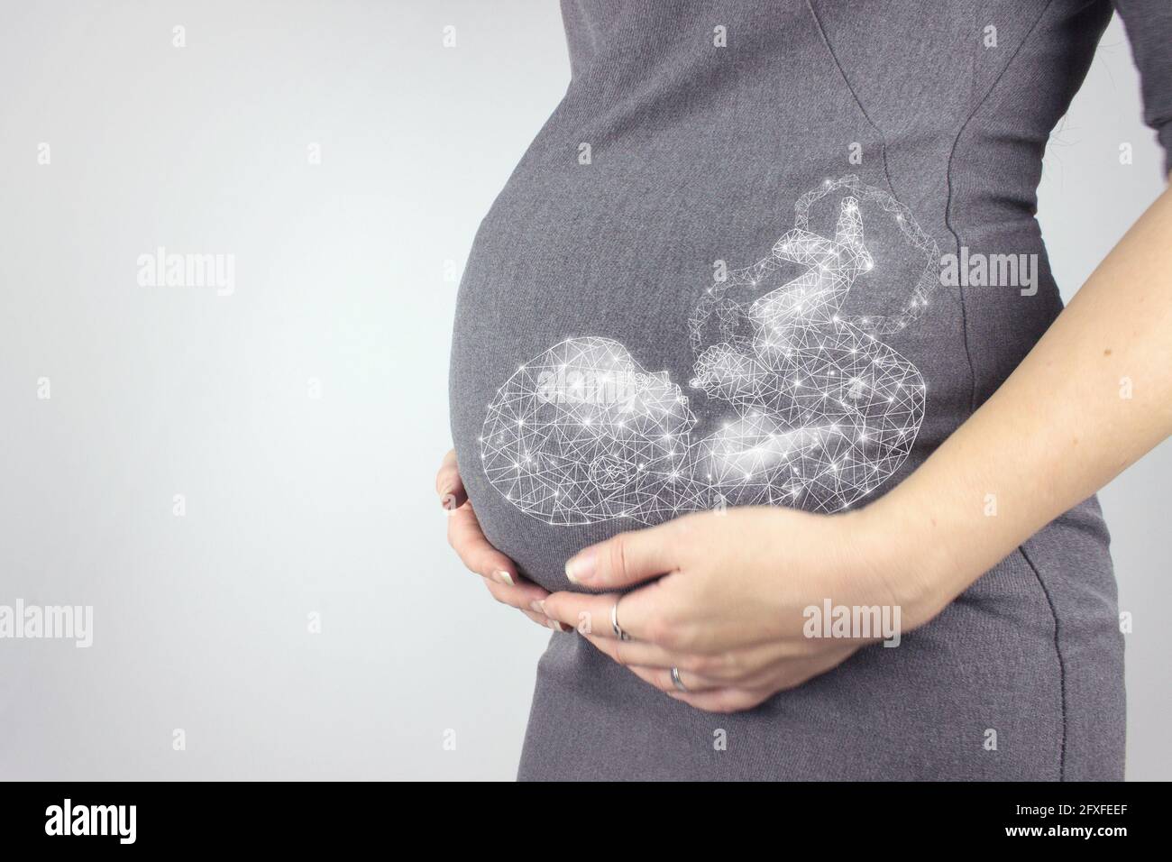 Femme enceinte en robe tient les mains sur le ventre avec un fœtus hologramme sur fond gris. Gros plan, espace de copie. Banque D'Images