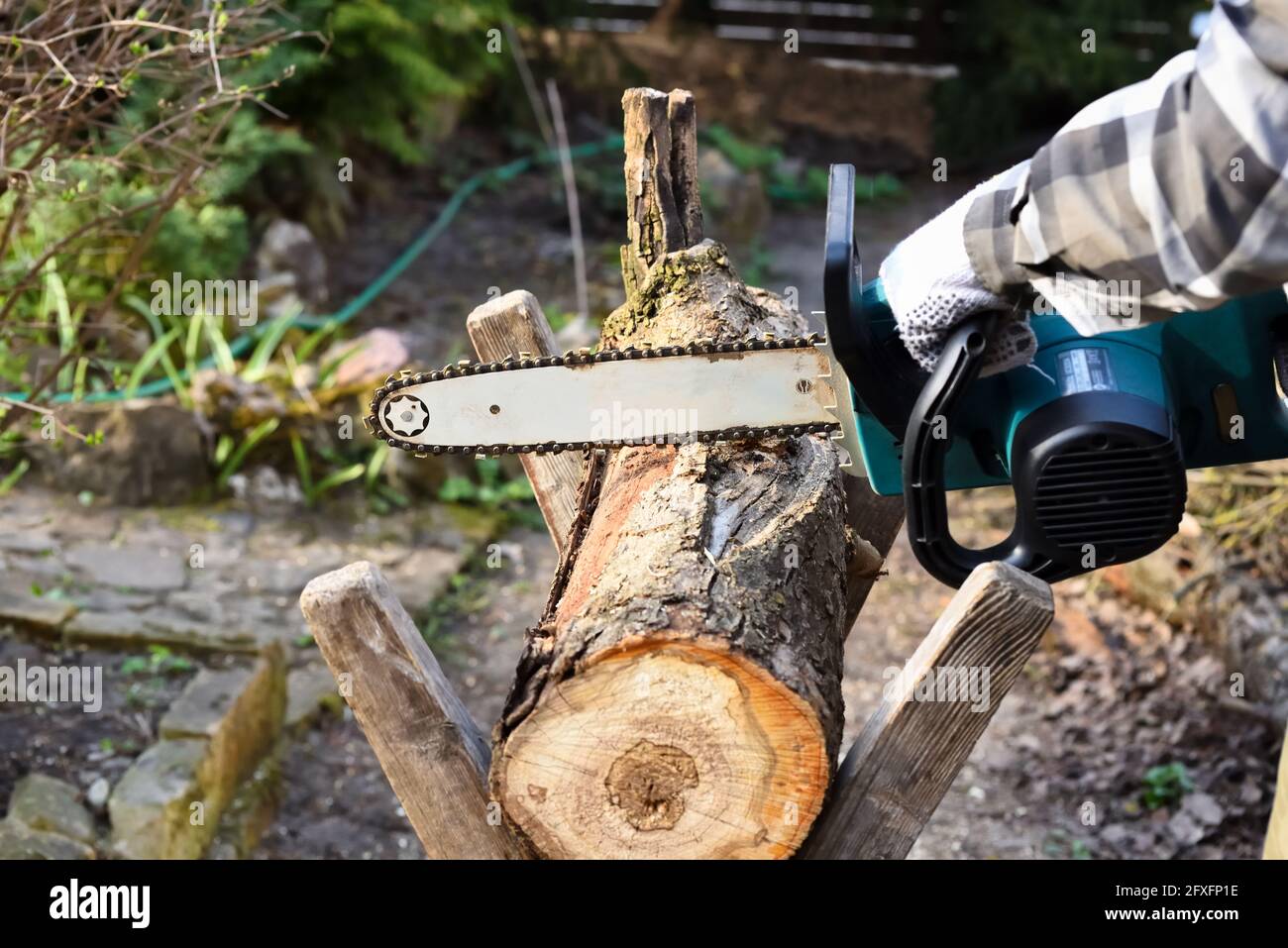 Tronçonneuse électrique dans les mains de l'homme tout en coupant une bûche pour le bois de chauffage. Travail saisonnier dans le jardin. Travailleur travaillant avec une scie dans le jardin. Banque D'Images