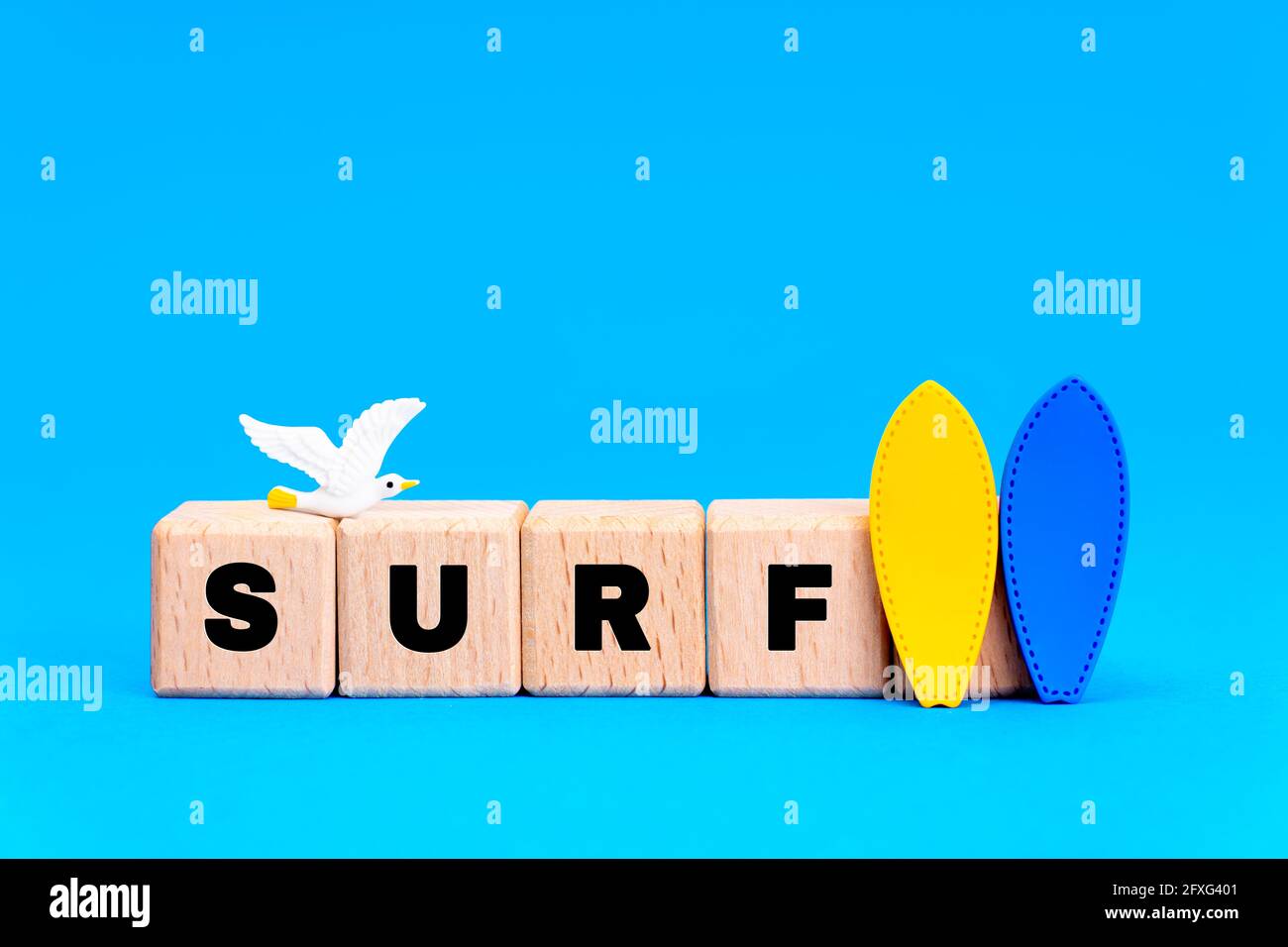 Word SURF fait de blocs d'alphabet en bois avec deux figurines de surf et un mouette sur fond bleu. Banque D'Images