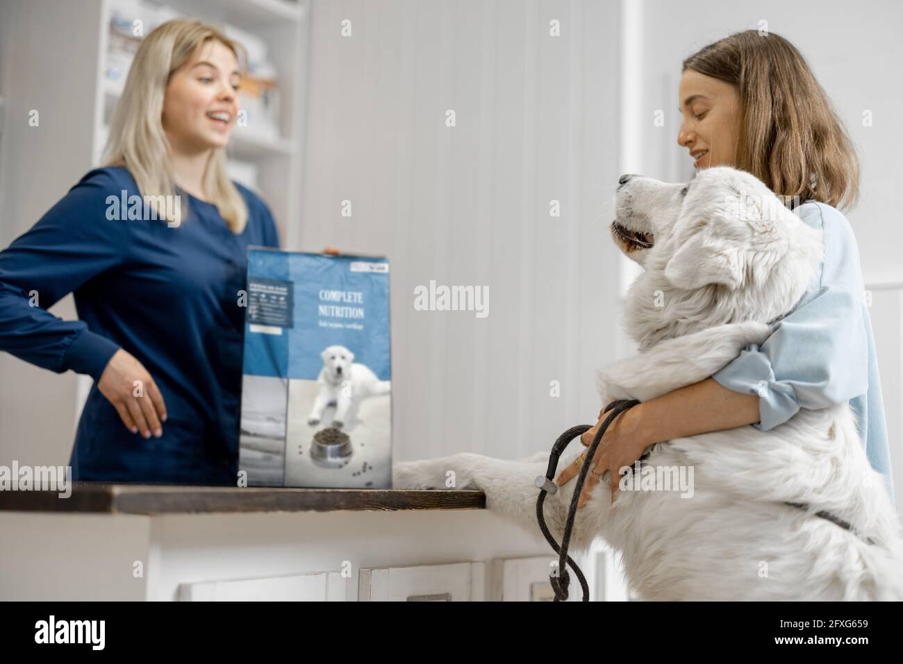 Femme propriétaire avec grand chien blanc à la réception dans la clinique vétérinaire choisir la nourriture sèche pour l'animal de compagnie. Le chien a grimpé les pattes sur la table. Soins et traitement pour animaux de compagnie Banque D'Images