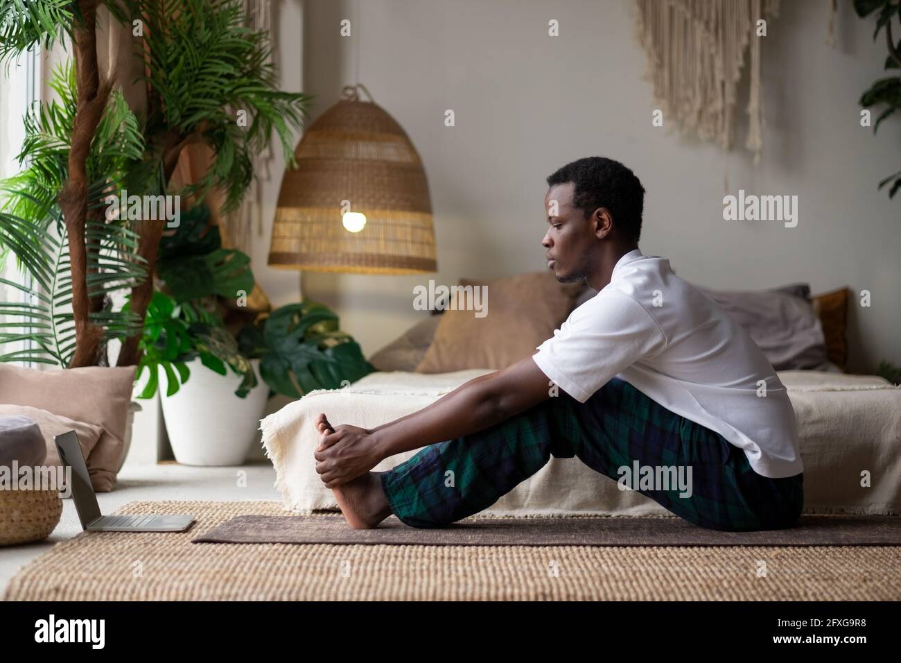 Jeune homme africain assis dans le paschimottanasana ou posture intense de l'étirement dorsal, assis dans la posture de la courbe vers l'avant, exercice pour les hanches et la colonne vertébrale à la maison Banque D'Images