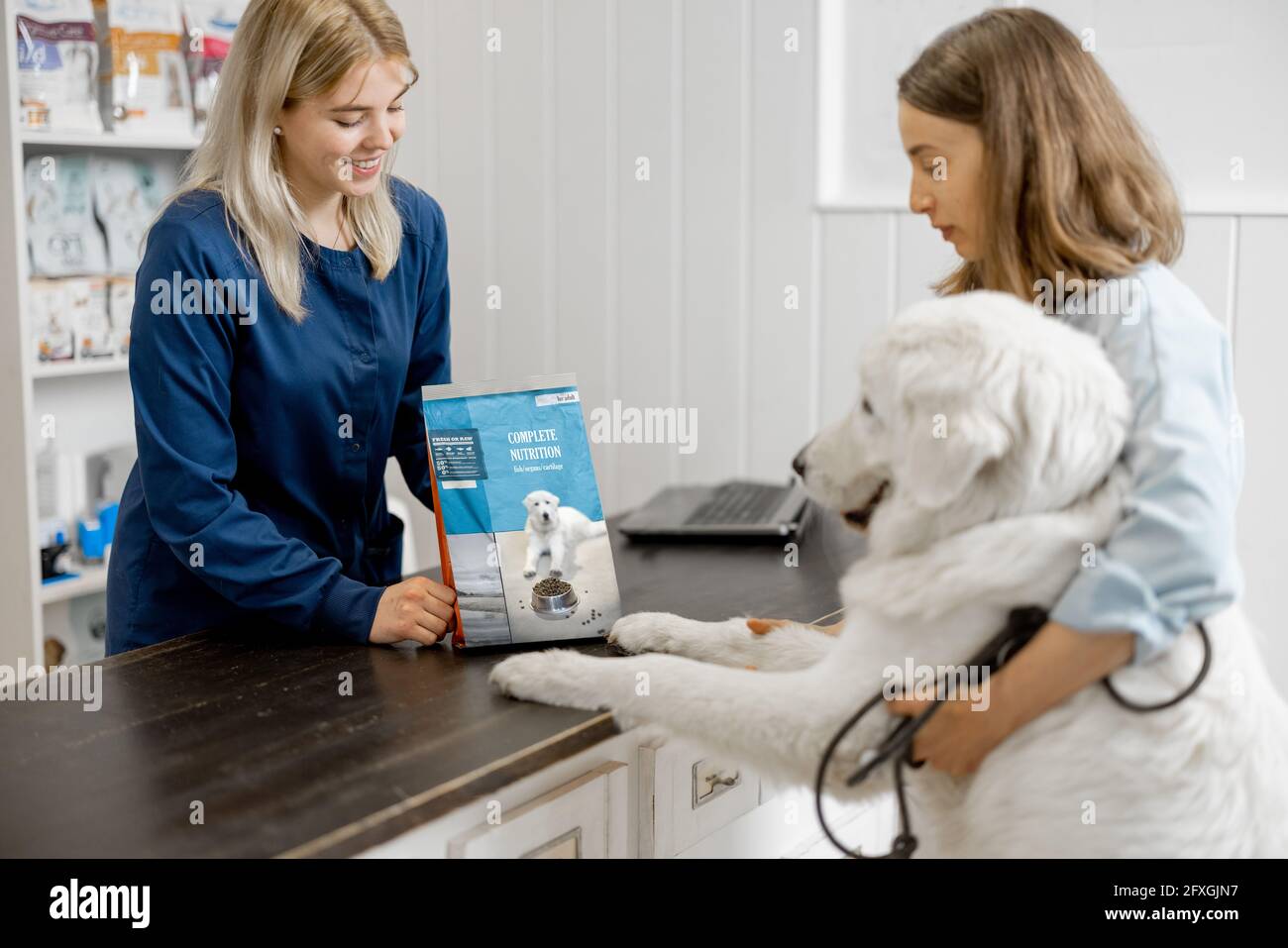 Femme propriétaire avec grand chien blanc à la réception dans la clinique vétérinaire choisir la nourriture sèche pour l'animal de compagnie. Le chien a grimpé les pattes sur la table. Soins et traitement pour animaux de compagnie Banque D'Images