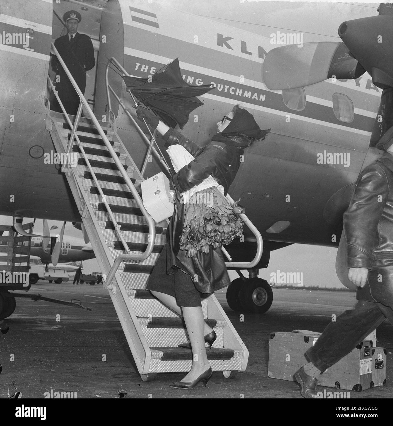 Scène de l'avion. Femme avec grand bouquet de fleurs. Son parapluie est  détruit par de forts vents], 15 avril 1963, fleurs, parapluies, Avions,  aéroports, pays-Bas, agence de presse du XXe siècle photo,