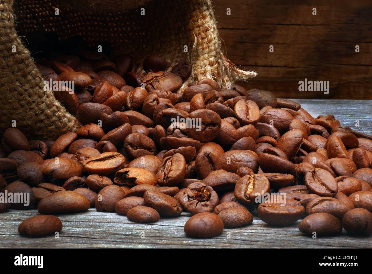 gros plan des grains de café torréfiés déversés dans le sac de toile de jute arrière-plan en bois Banque D'Images