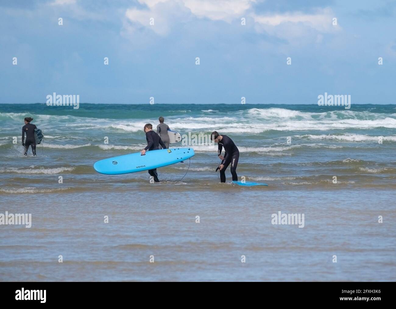 Un groupe de jeunes amis masculins portant leurs planches de surf embauchées Marche dans la mer à Mawgan Porth pour commencer un Session de surf sur une marche de Cornish Banque D'Images