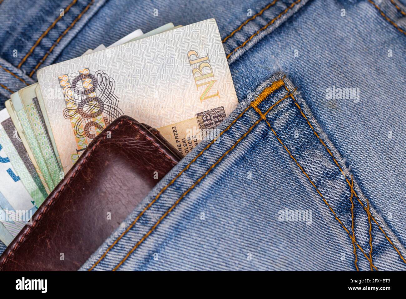 Portefeuille et beaucoup de billets polonais sortant de la poche arrière du pantalon en denim. Photo prise sous une lumière artificielle douce Banque D'Images