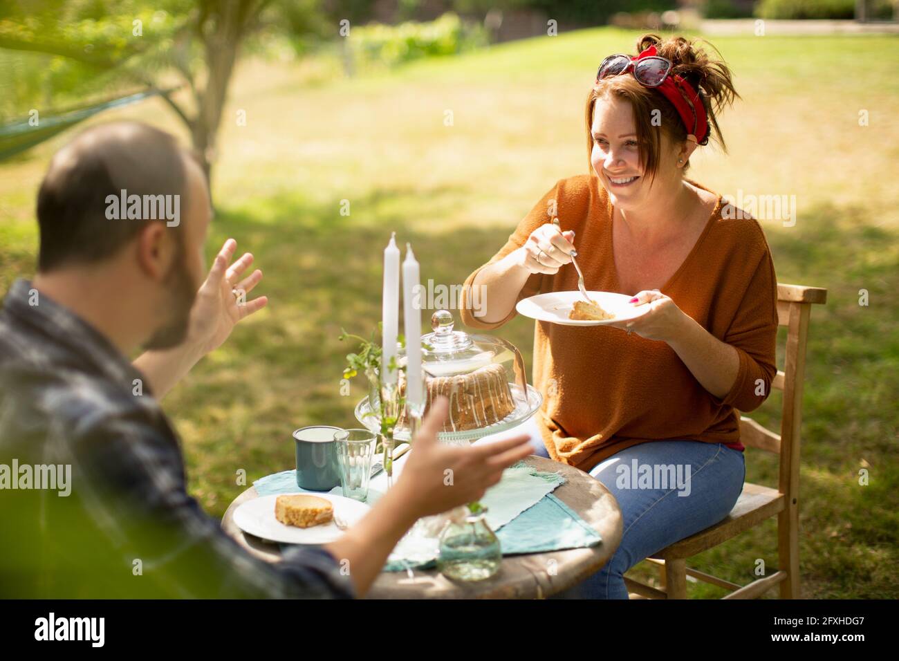 Couple heureux en train de déguster un gâteau et un thé à la table ensoleillée du jardin Banque D'Images