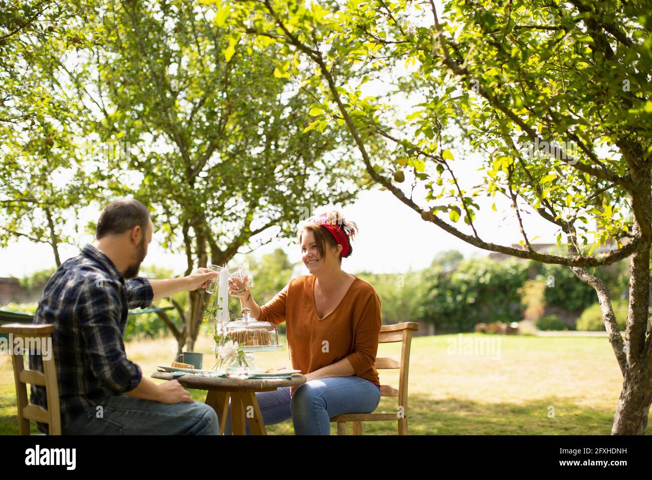 Couple heureux de déguster des verres d'eau à table dans le jardin d'été ensoleillé Banque D'Images