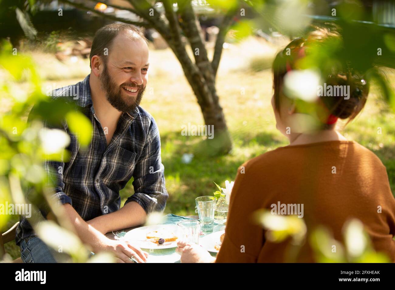 Couple heureux en train de déguster un gâteau à table dans un jardin d'été ensoleillé Banque D'Images Couple heureux en train de déguster un gâteau à table dans un jardin d'été ensoleillé Banque D'Images