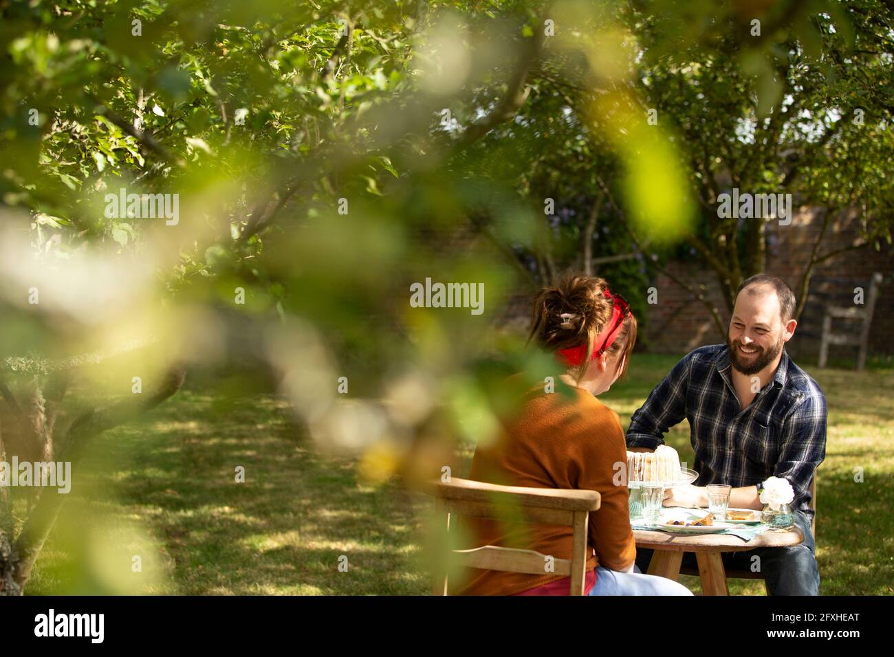 Couple dégustant un gâteau à table dans un verger ensoleillé d'été Banque D'Images Couple dégustant un gâteau à table dans un verger ensoleillé d'été Banque D'Images
