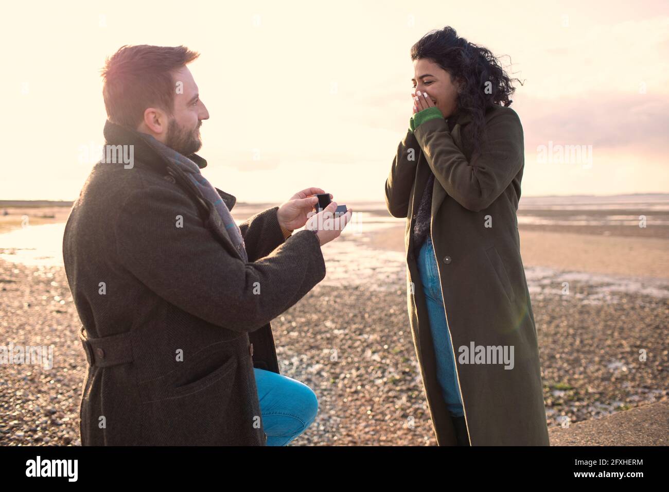 Homme proposant à sa petite amie sur une plage ensoleillée d'hiver Banque D'Images