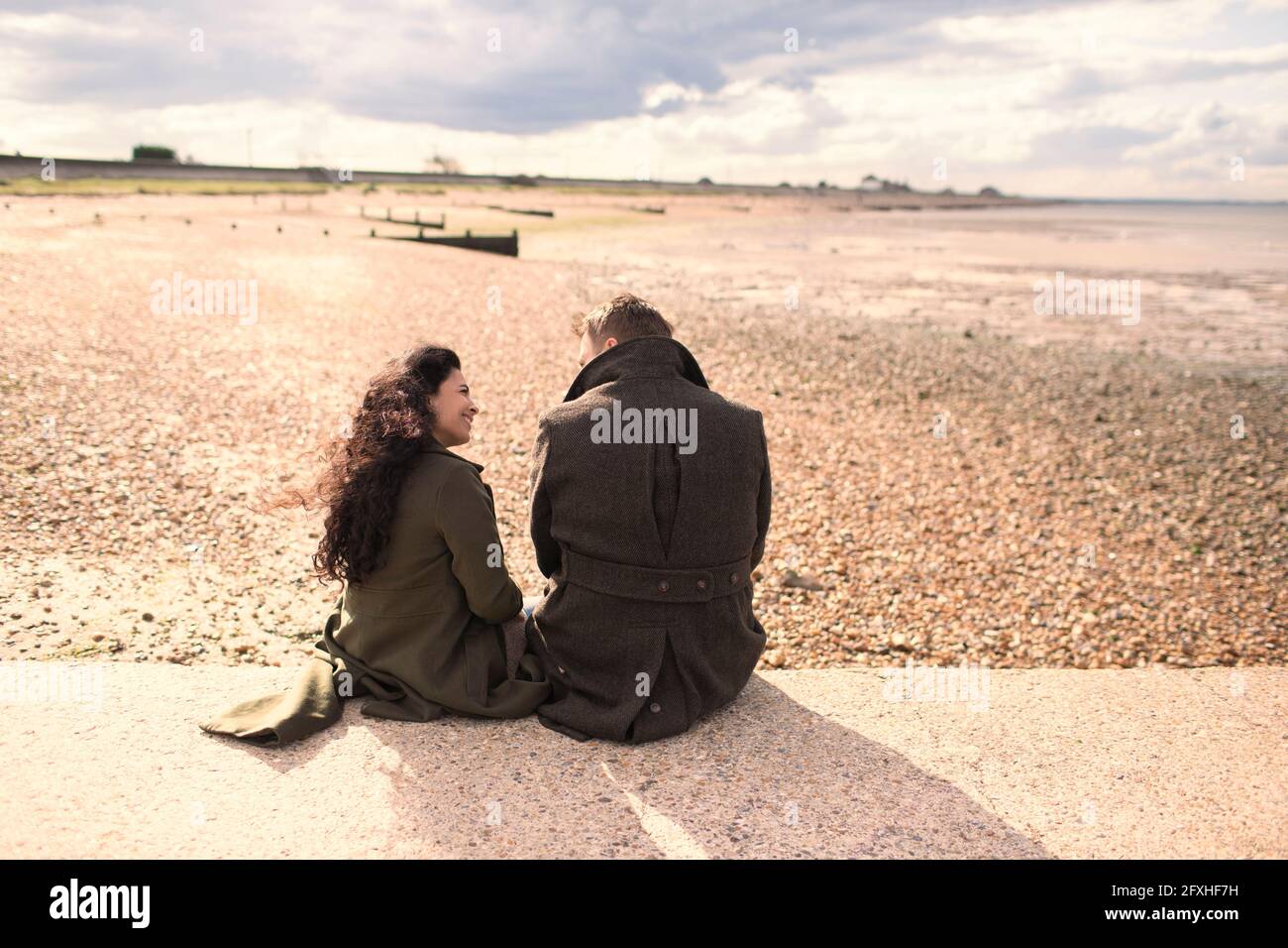 Couple en manteau d'hiver sur la plage ensoleillée Banque D'Images