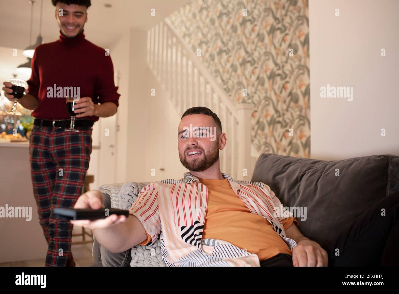 Un couple gay masculin avec un téléviseur qui regarde le vin à la maison Banque D'Images