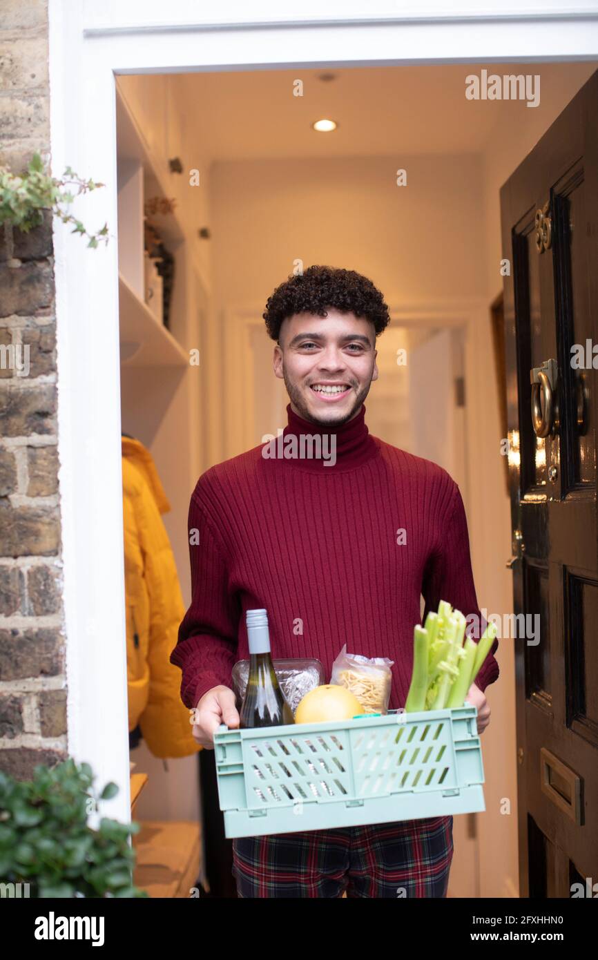 Portrait un jeune homme heureux qui reçoit une livraison d'épicerie à la porte d'entrée Banque D'Images