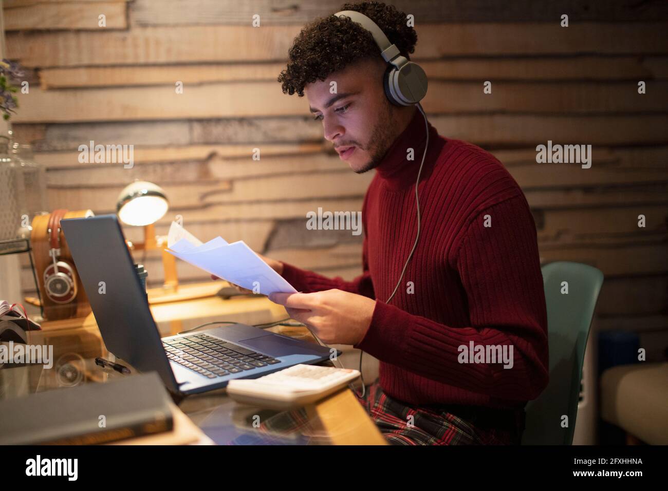 Jeune homme avec des écouteurs et de la paperasserie travaillant tard à la maison Banque D'Images