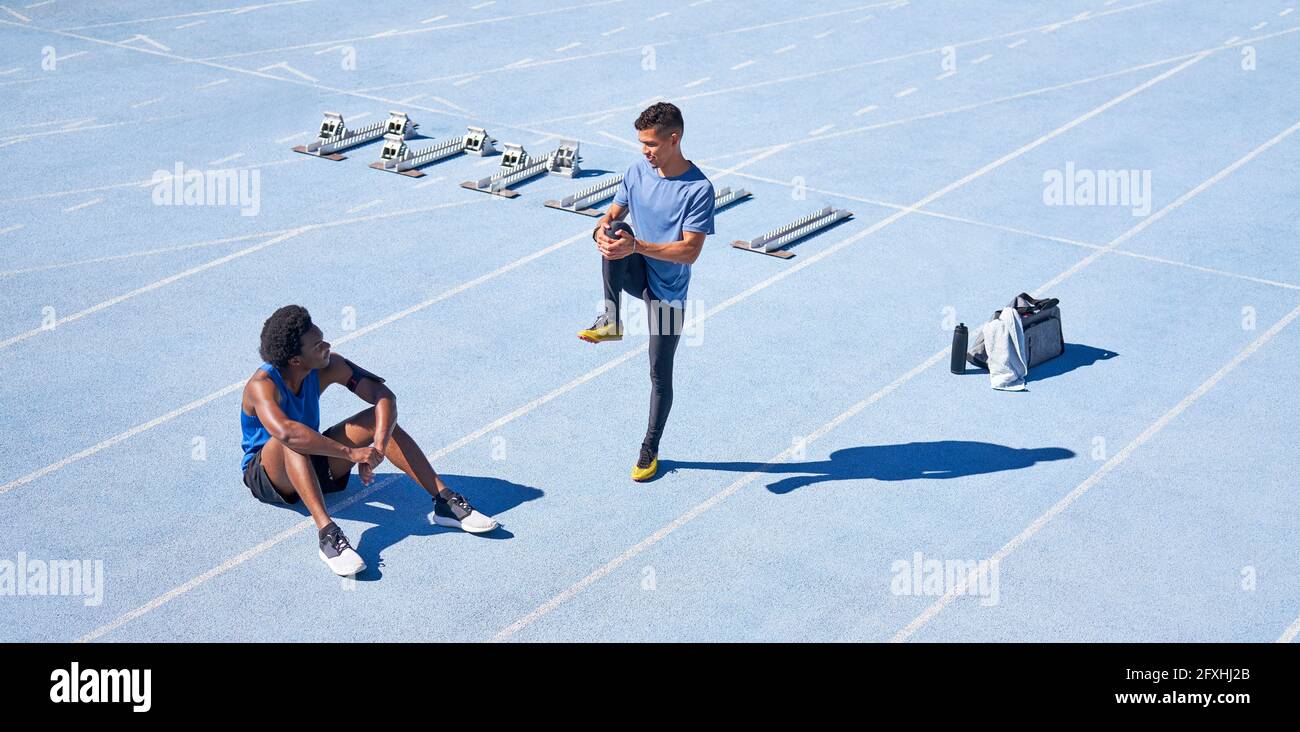 Jeunes coureurs masculins sur piste de sport bleu ensoleillé Banque D'Images