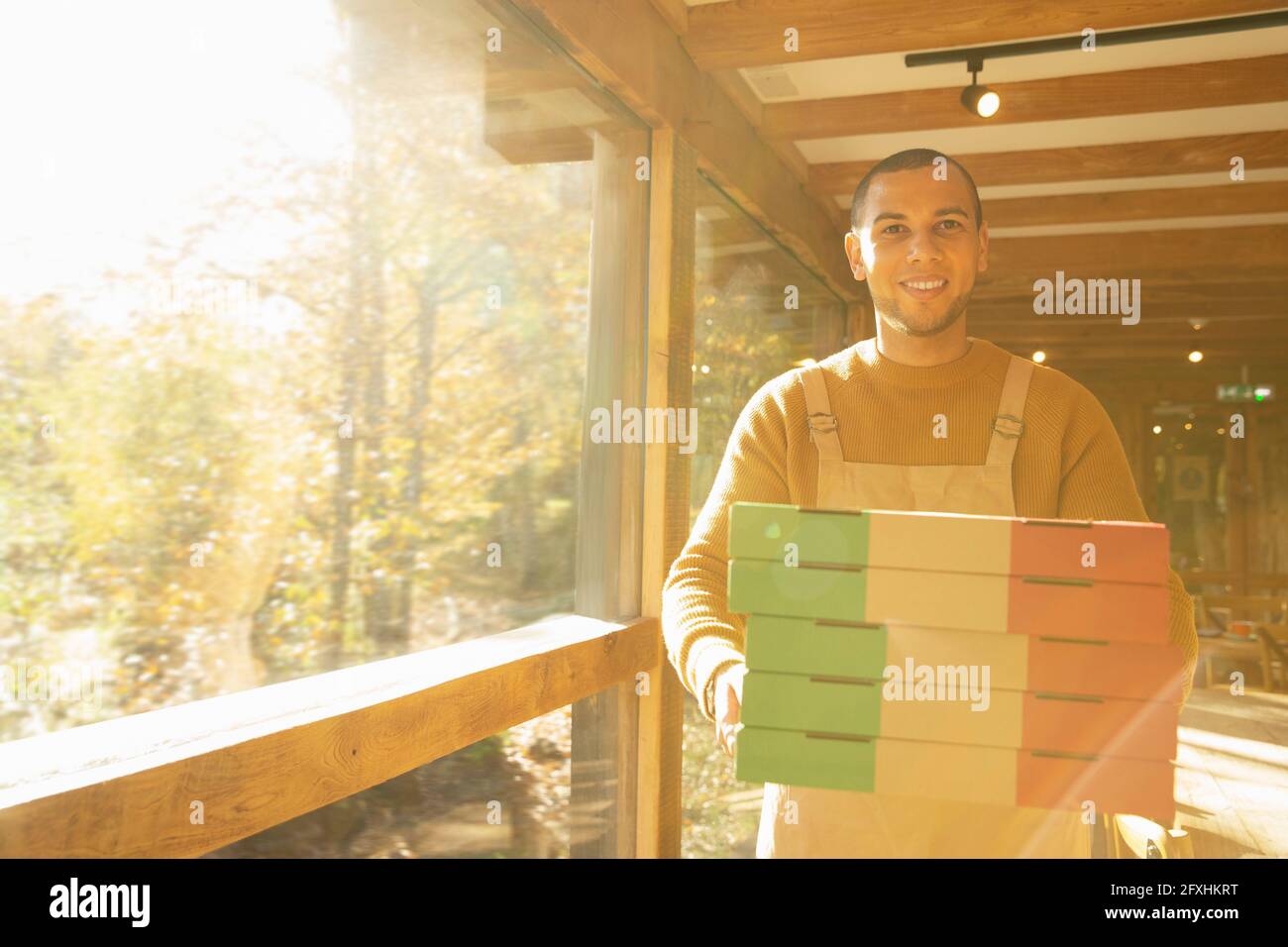Portrait fier propriétaire de pizzeria mâle avec des boîtes à pizza à la fenêtre ensoleillée Banque D'Images