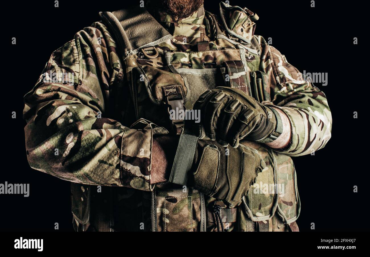 Photo d'un soldat dans un gilet blindé camouflé de niveau 3 mettant des gants tactiques sur fond noir. Banque D'Images