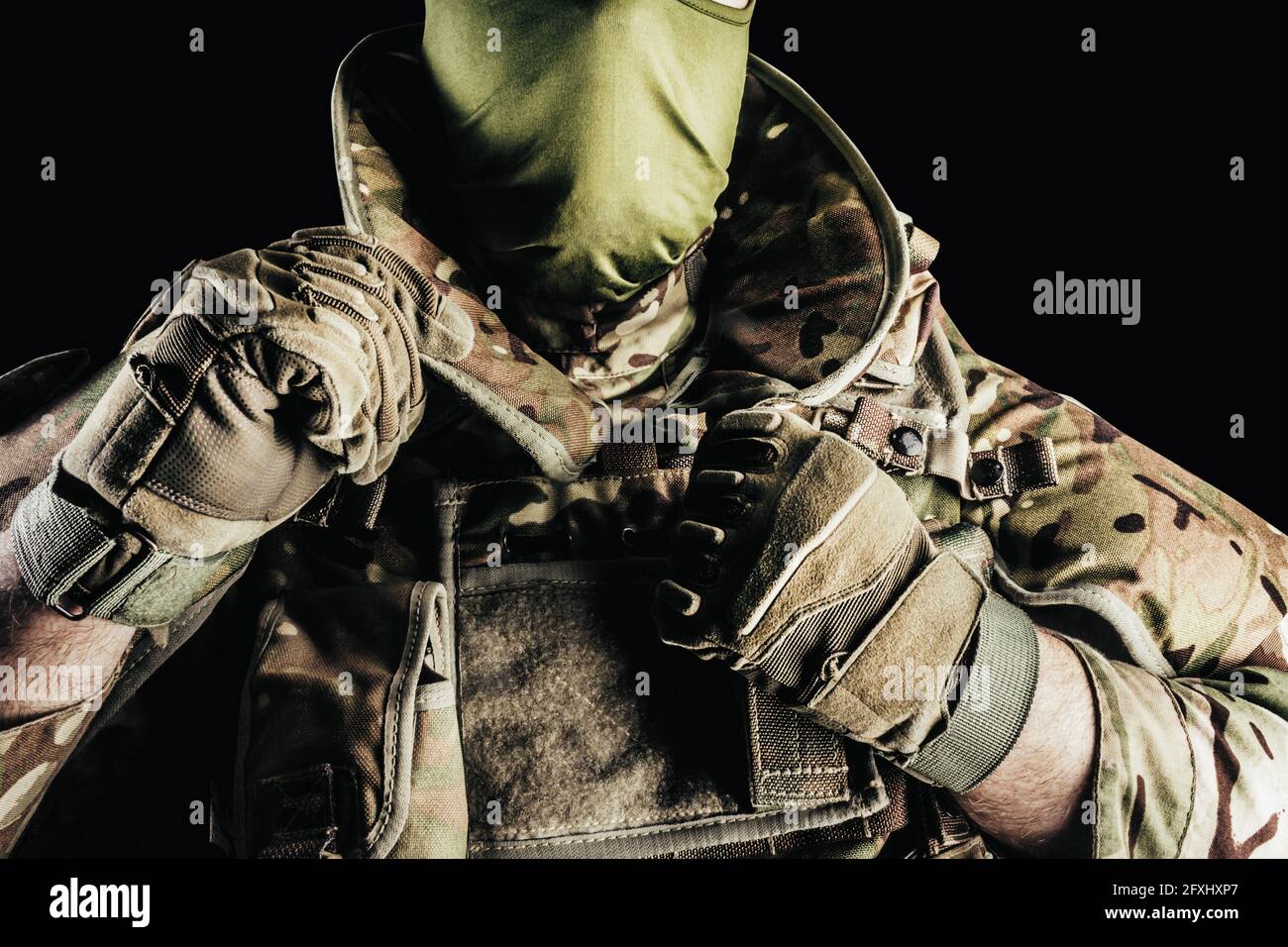 Photo d'un soldat dans des munitions de gilet blindé de niveau 3, gants tactiques mettant sur la protection du cou sur fond noir. Banque D'Images