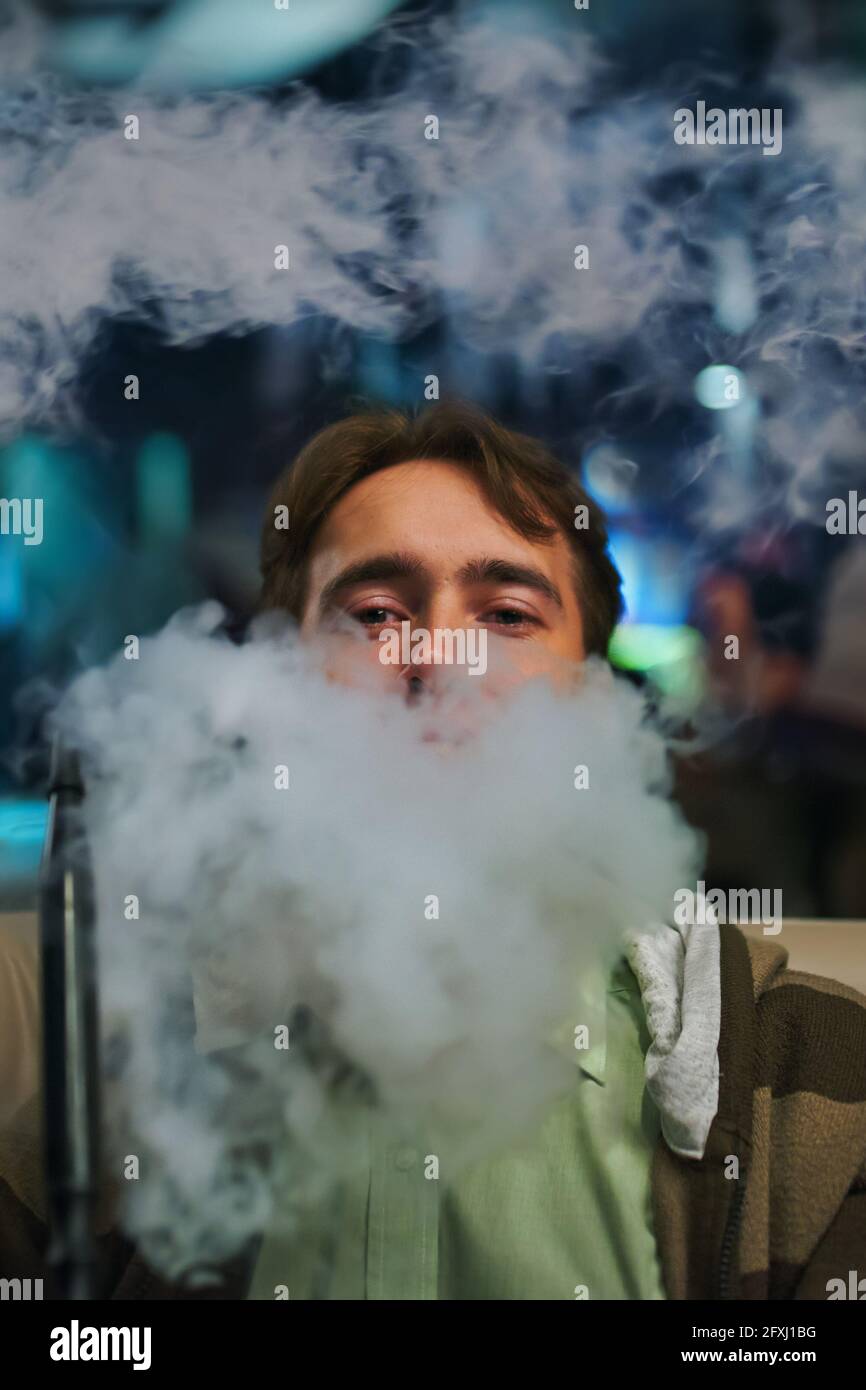 Portrait d'un jeune homme dans la fumée. Homme au restaurant fumant le narguilé. Personne sur le canapé dans le café. Détendez-vous au bar shisha. Banque D'Images