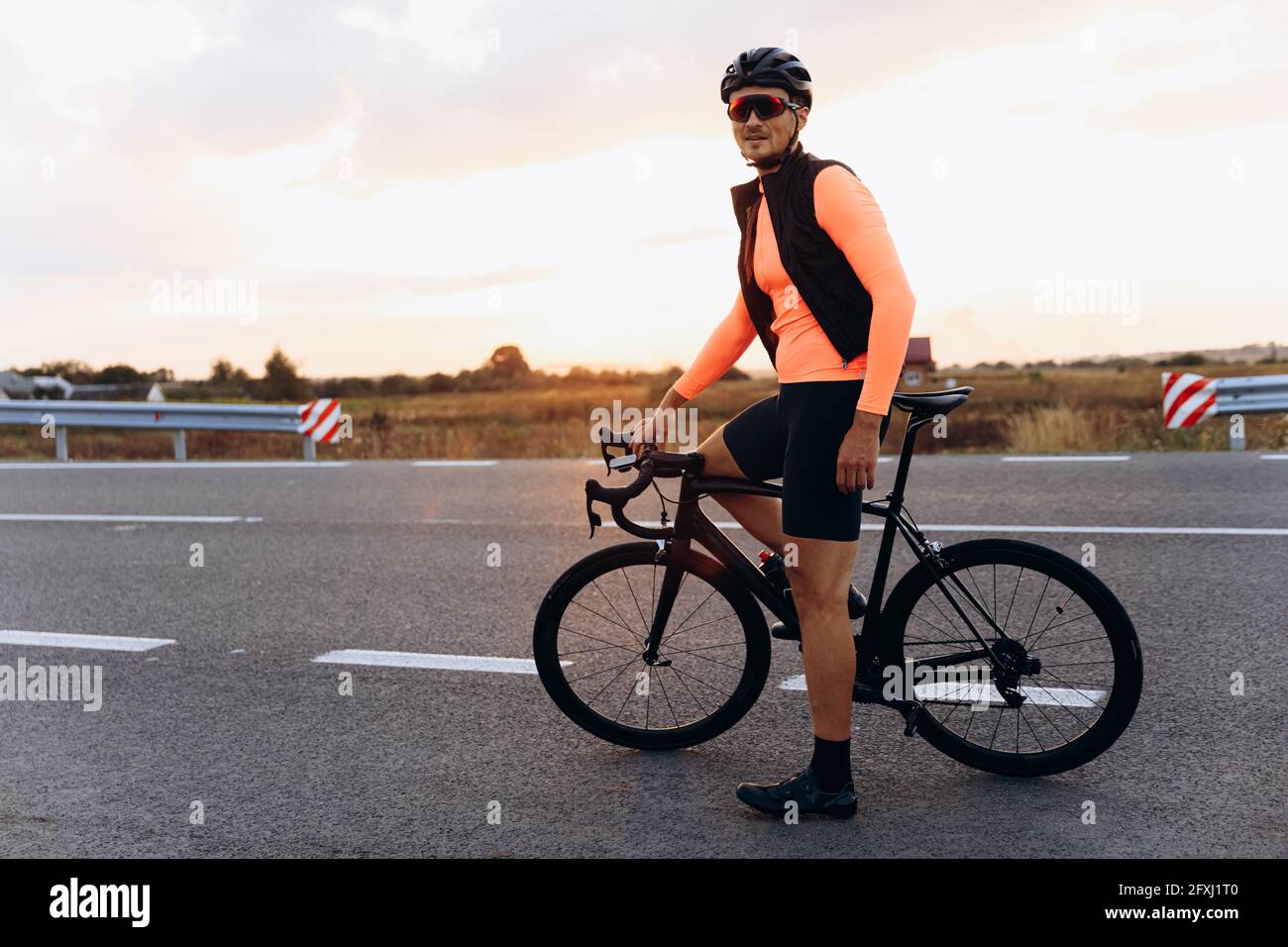 Jeune cycliste heureux posant avec un vélo sur une route pavée Banque D'Images