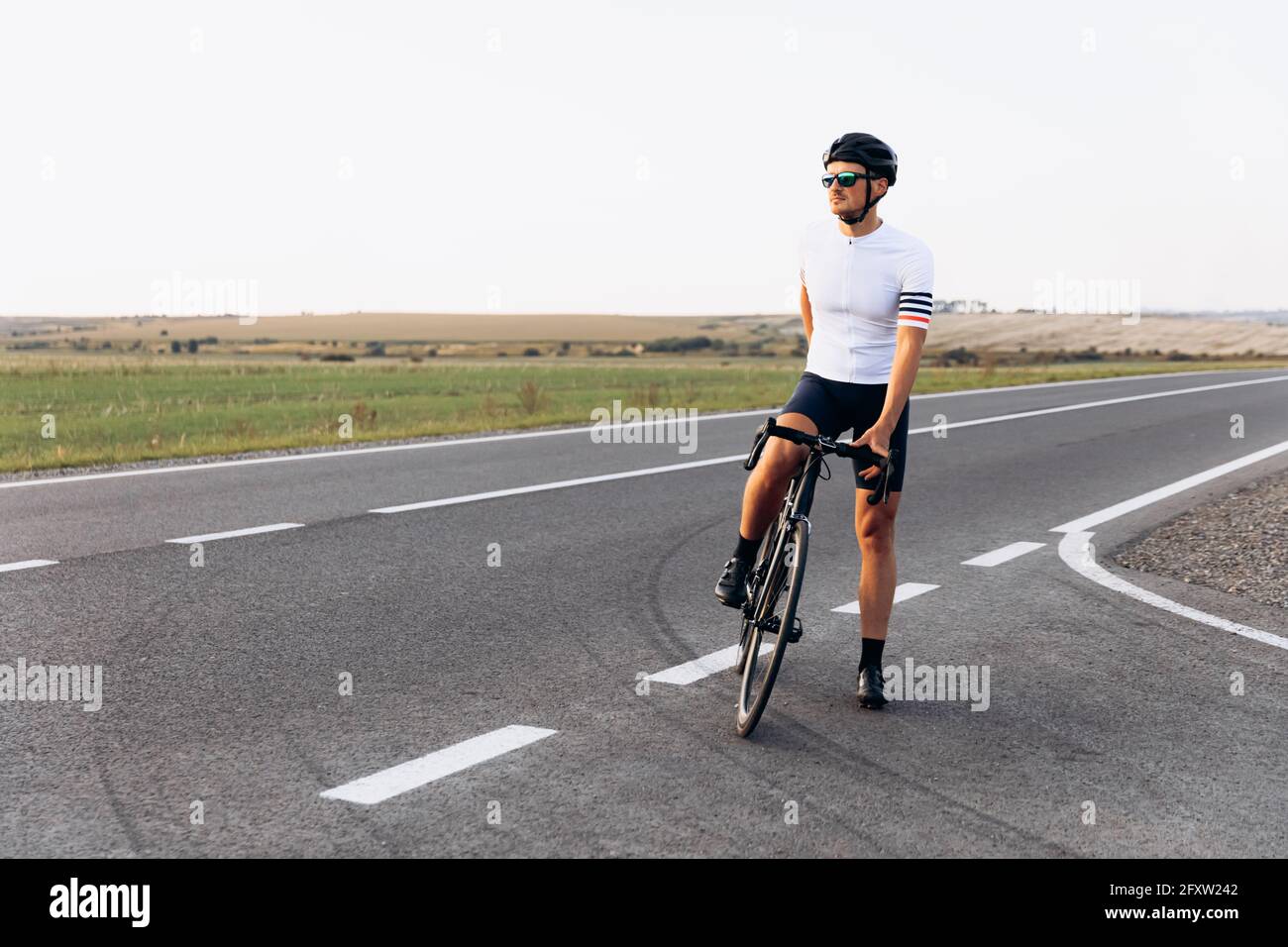 Homme barbu dans une tenue de sport se détendant sur la route avec un vélo Banque D'Images