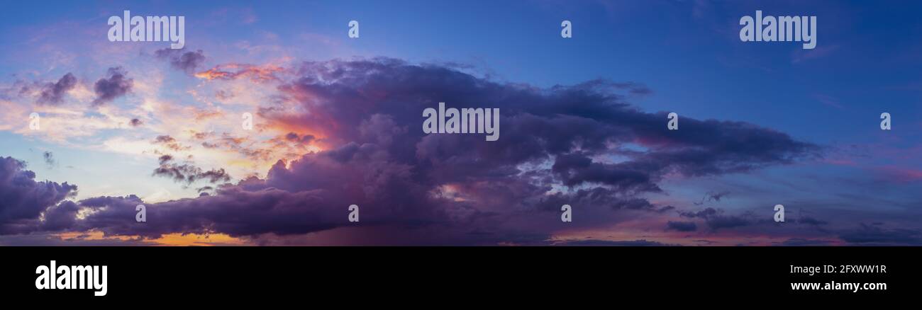 Grand panorama avec ciel bleu vif et coucher de soleil spectaculaire contrastant les couleurs jaune, rouge et orange touchant le cumulus nuage. Banque D'Images