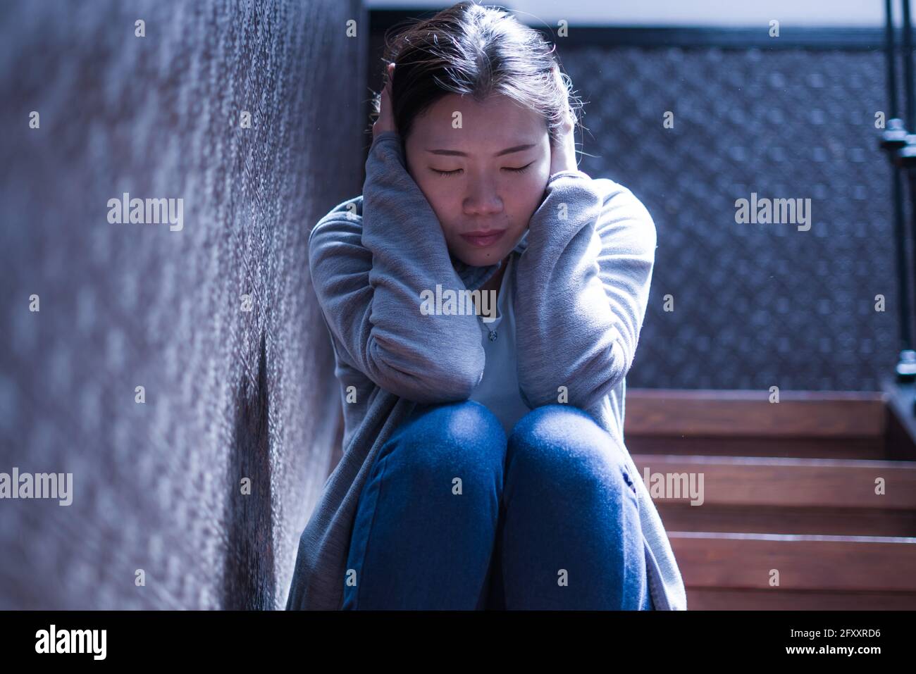 Jeune belle femme asiatique dans la douleur souffrant de dépression - dramatique Portrait à l'intérieur sur l'escalier d'une fille chinoise triste et déprimée comme victime de l'intimidation Banque D'Images
