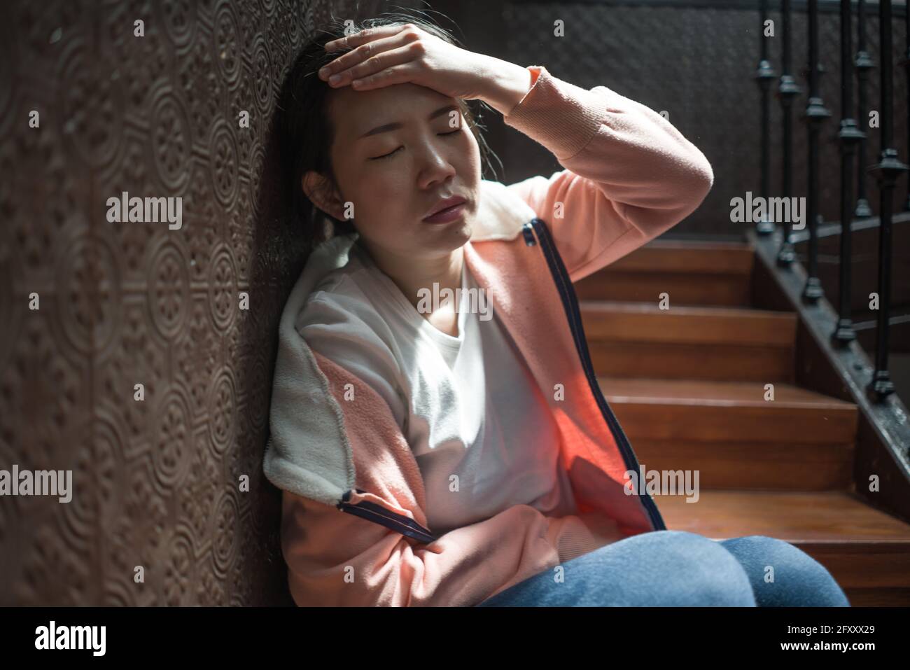 Jeune belle femme asiatique dans la douleur souffrant de dépression - dramatique Portrait à l'intérieur sur l'escalier d'une fille japonaise triste et déprimée comme victime de taureau Banque D'Images