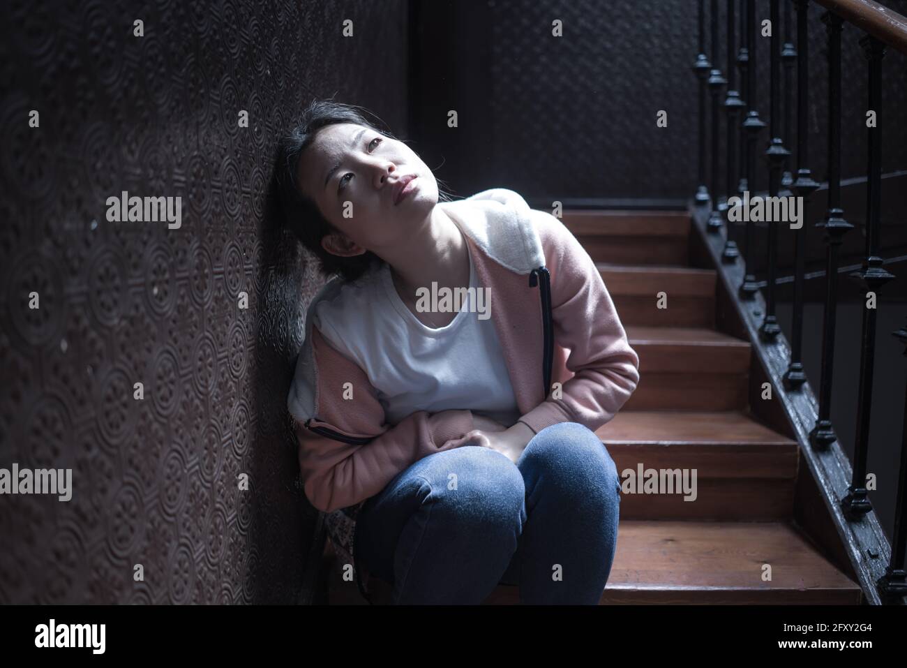 Jeune belle femme asiatique dans la douleur souffrant de dépression - dramatique Portrait à l'intérieur sur l'escalier d'une fille coréenne triste et déprimée comme victime de bullyi Banque D'Images