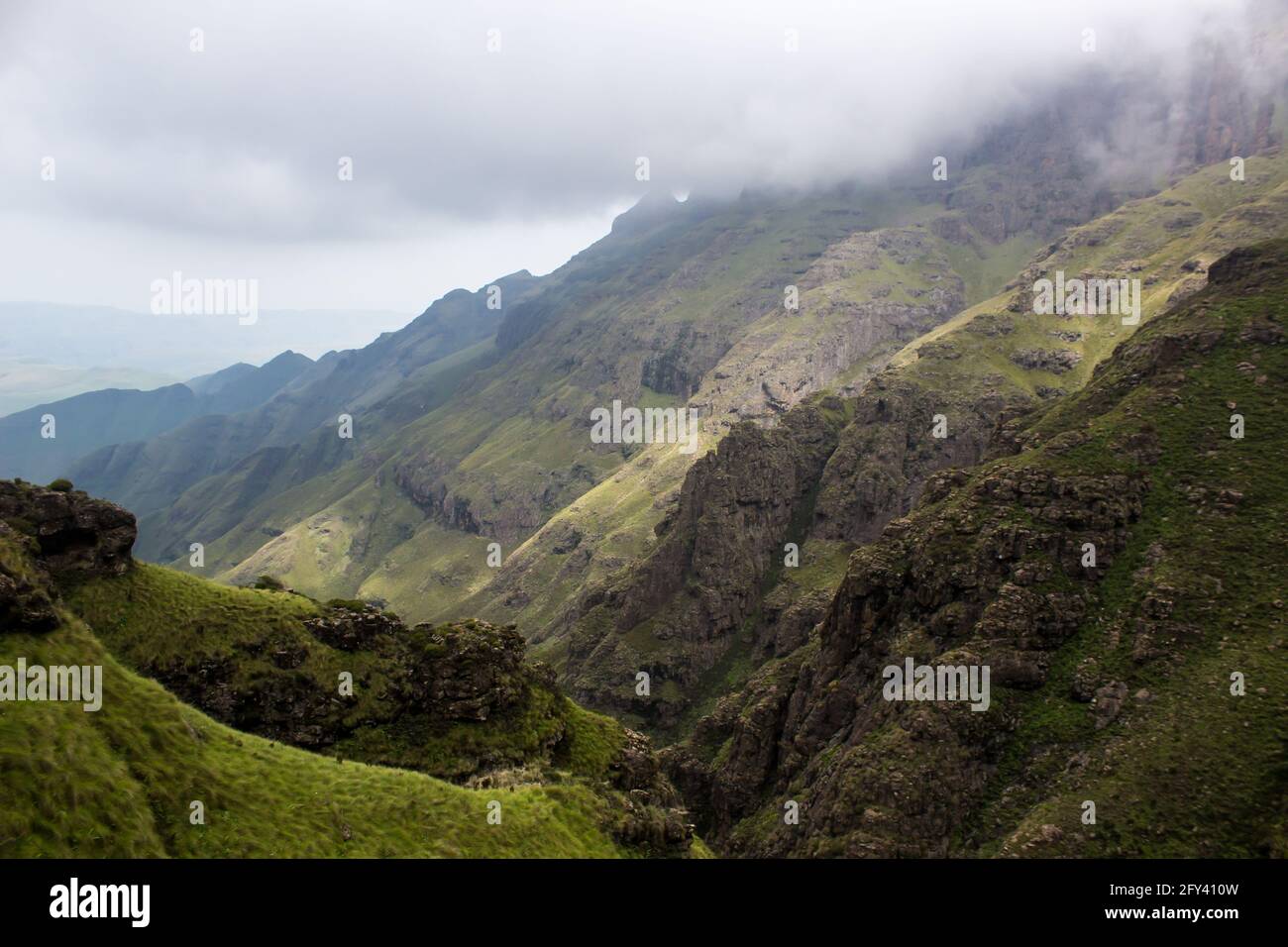 Nuages descendant dans une vallée étroite dans les montagnes accidentées et élevées du Drakensberg. Les falaises et les pics emblématiques des montagnes du Drakensberg se sont formés pendant Banque D'Images