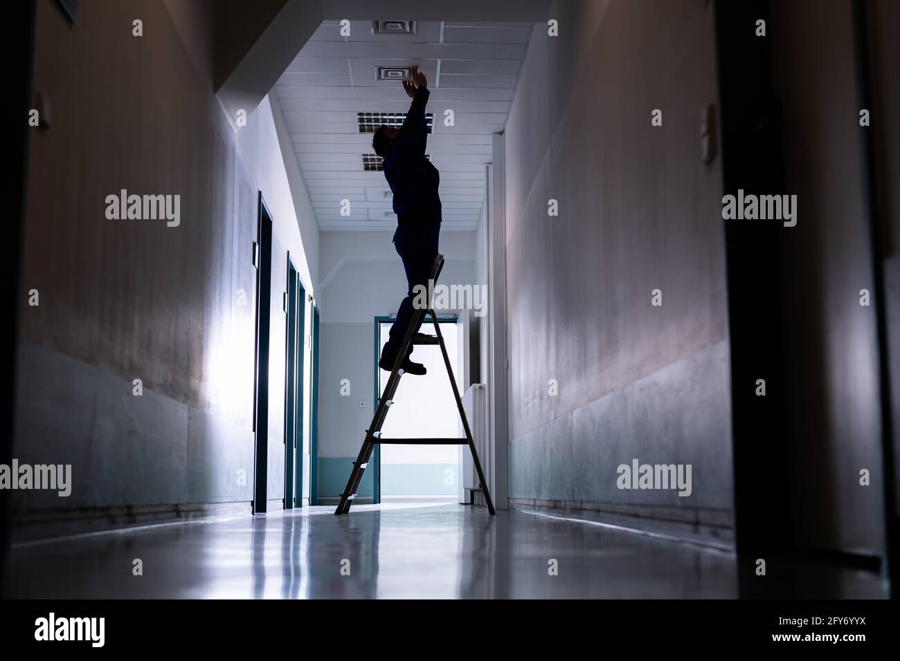 Le technicien répare les présentoirs de plafond dans le bureau sur le escabeau Banque D'Images