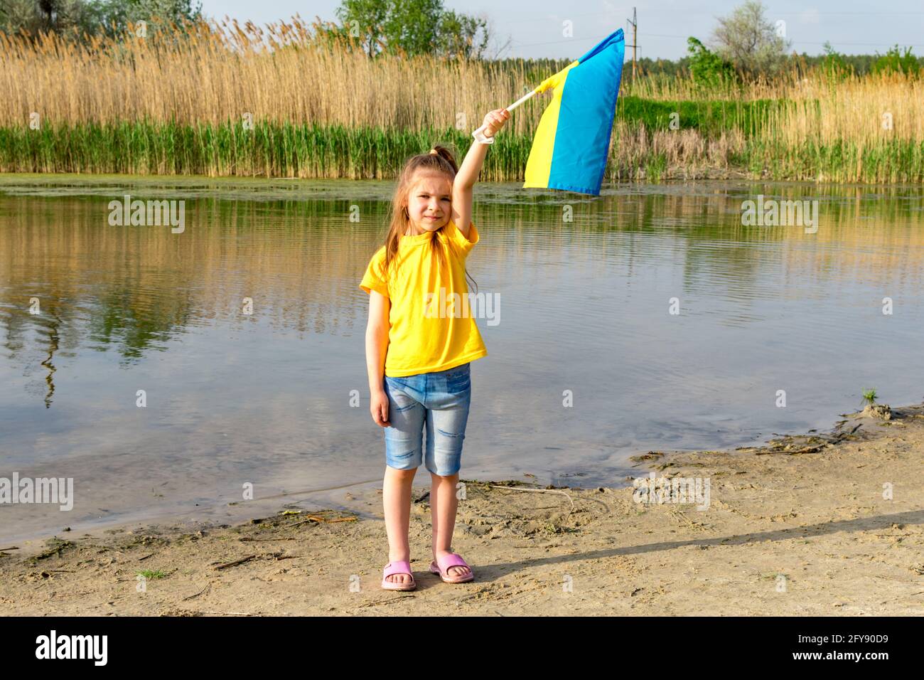 Le drapeau de l'Ukraine flotte entre les mains d'une petite fille sur fond de lac. Jour de l'indépendance de l'Ukraine et jour du drapeau. Banque D'Images