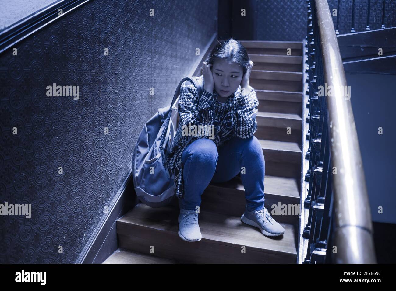 Jeune belle femme asiatique dans la douleur souffrant de dépression - dramatique Portrait à l'intérieur sur l'escalier d'une fille japonaise triste et déprimée comme victime de taureau Banque D'Images