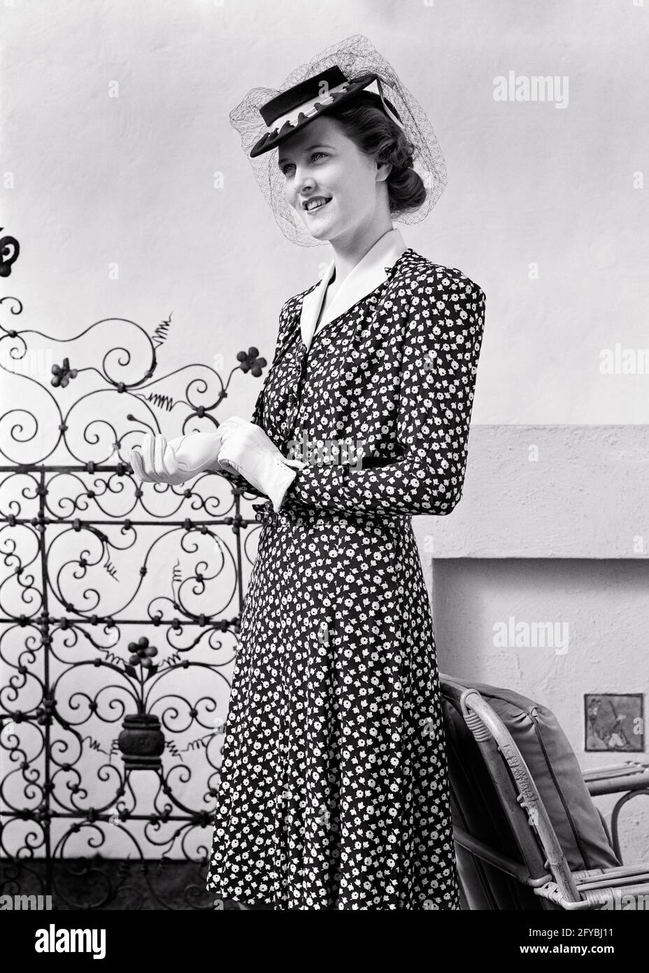 FEMME BRUNETTE CHIC ET TENDANCE DES ANNÉES 1940 PORTANT UNE ROBE À IMPRIMÉ  AVEC GANTS À COL BLANC ET CHAPEAU PERKY AVEC VOILE EN FILET - G1027 HAR001  HARS DEMI-LONGUEUR FEMMES PERSONNES