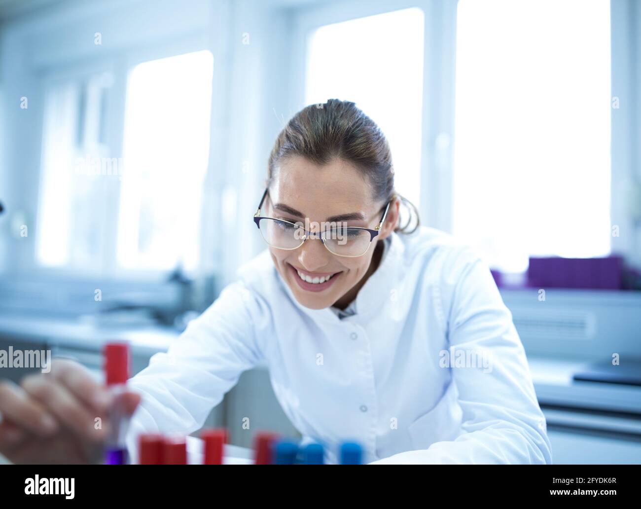 Jeune technicien de laboratoire scientifique travaillant en tenant un flacon souriant. Femme satisfaite dans un hôpital de laboratoire faisant des expériences de recherche. Banque D'Images