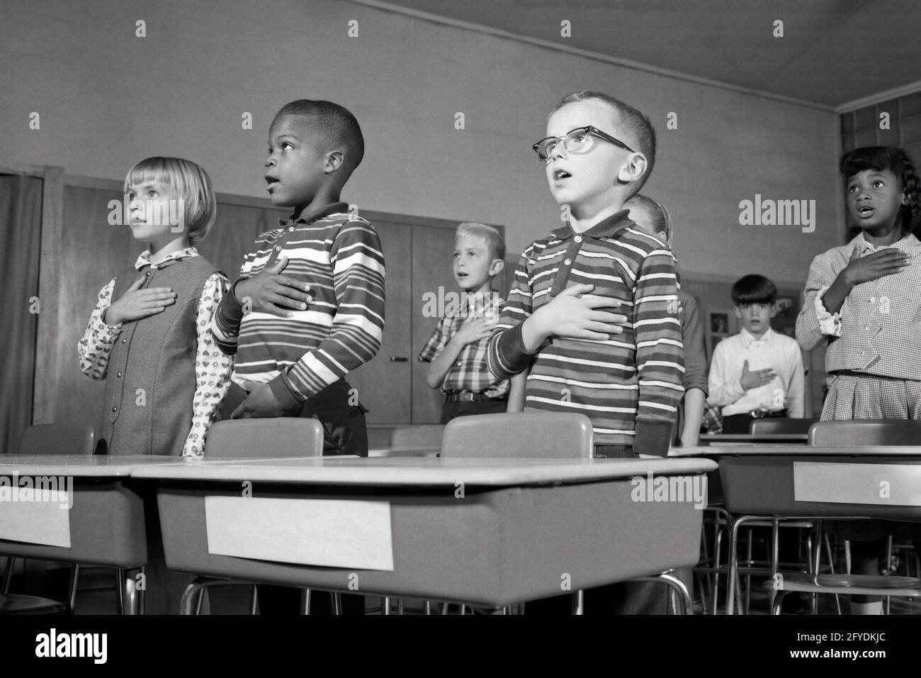 LES ENFANTS DE L'ÉCOLE DES ANNÉES 1960 DEBOUT À DES BUREAUX DISANT PROMESSE DE ALLÉGEANCE AU DRAPEAU DES ÉTATS-UNIS AVEC LES MAINS SUR LEUR COEUR - S15673 HAR001 HARS DEMI-LONGUEUR INSPIRATION ÉTATS-UNIS D'AMÉRIQUE HOMMES SIX BUREAUX B&W ÉCOLES NORD-AMÉRICAINES FREEDOM GRADE COEURS AFRO-AMÉRICAINS AFRO-AMÉRICAINS BAS ANGLE NOIR FIERTÉ INTÉGRÉE PATRIOT PATRIOTE PRIMAIRE PATRIOTE DIVERS COOPÉRATION SCOLAIRE DE CROISSANCE JUVÉNILES UN SERMENT D'ALLÉGEANCE PATRIOTIQUE RÉCITANT L'APPARTENANCE ETHNIQUE BLANCHE ET NOIRE HAR001 AFRO-AMÉRICAINS À L'ANCIENNE Banque D'Images