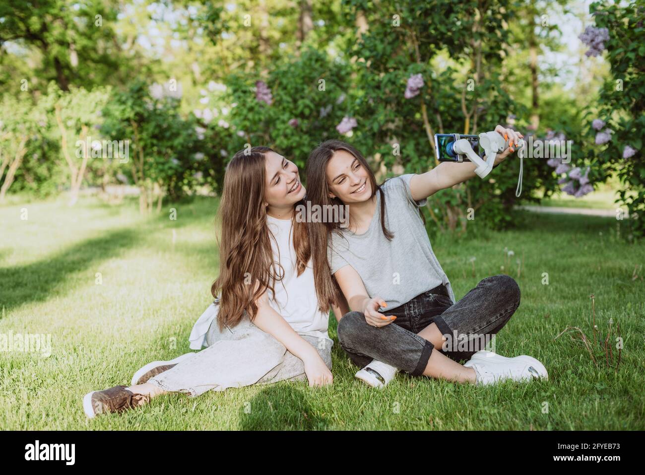 Souriantes, les blogueurs d'influenceurs sont en train de filmer ou d'enregistrer de la vidéo avec leur smartphone sur un stabilisateur, dans un parc vert ensoleillé à l'extérieur. BL Banque D'Images