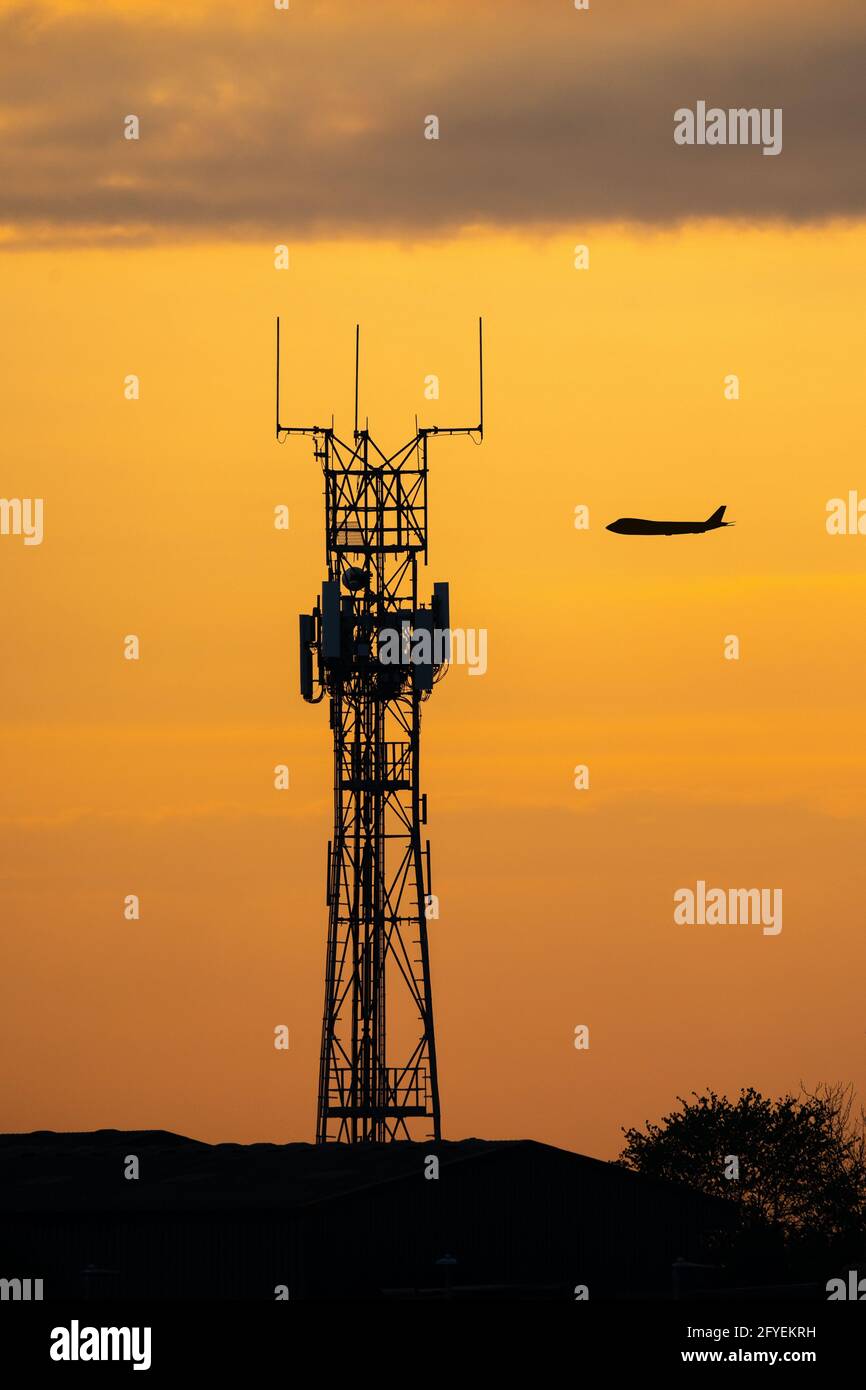 Silhouette de jumbo-jet volant au coucher du soleil derrière un mât de radio de haute technologie pour les communications entre le pilote et l'aéroport. Communications de contrôle de la circulation aérienne avec or Banque D'Images