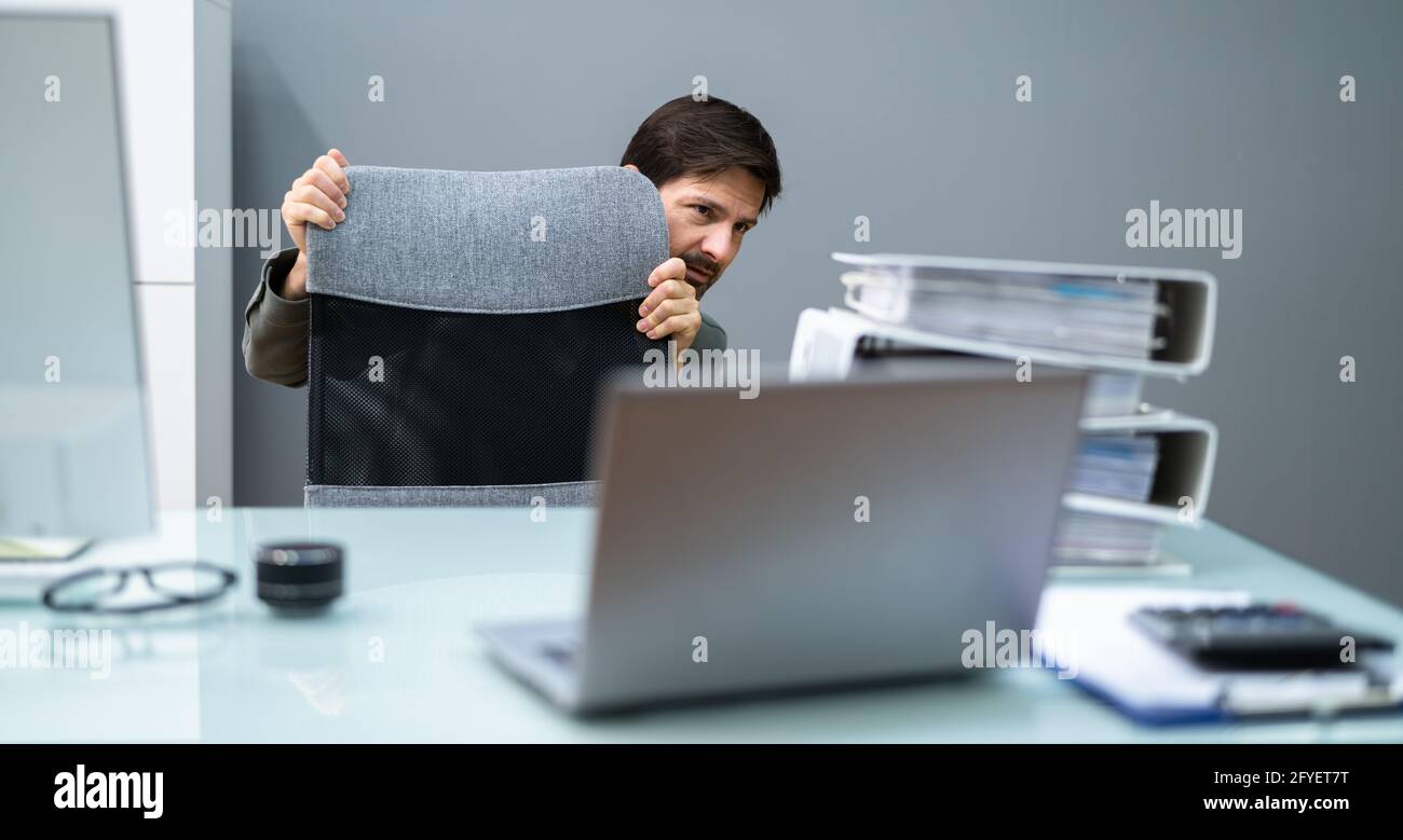 Un homme effrayé se cache derrière le bureau dans la chambre Banque D'Images