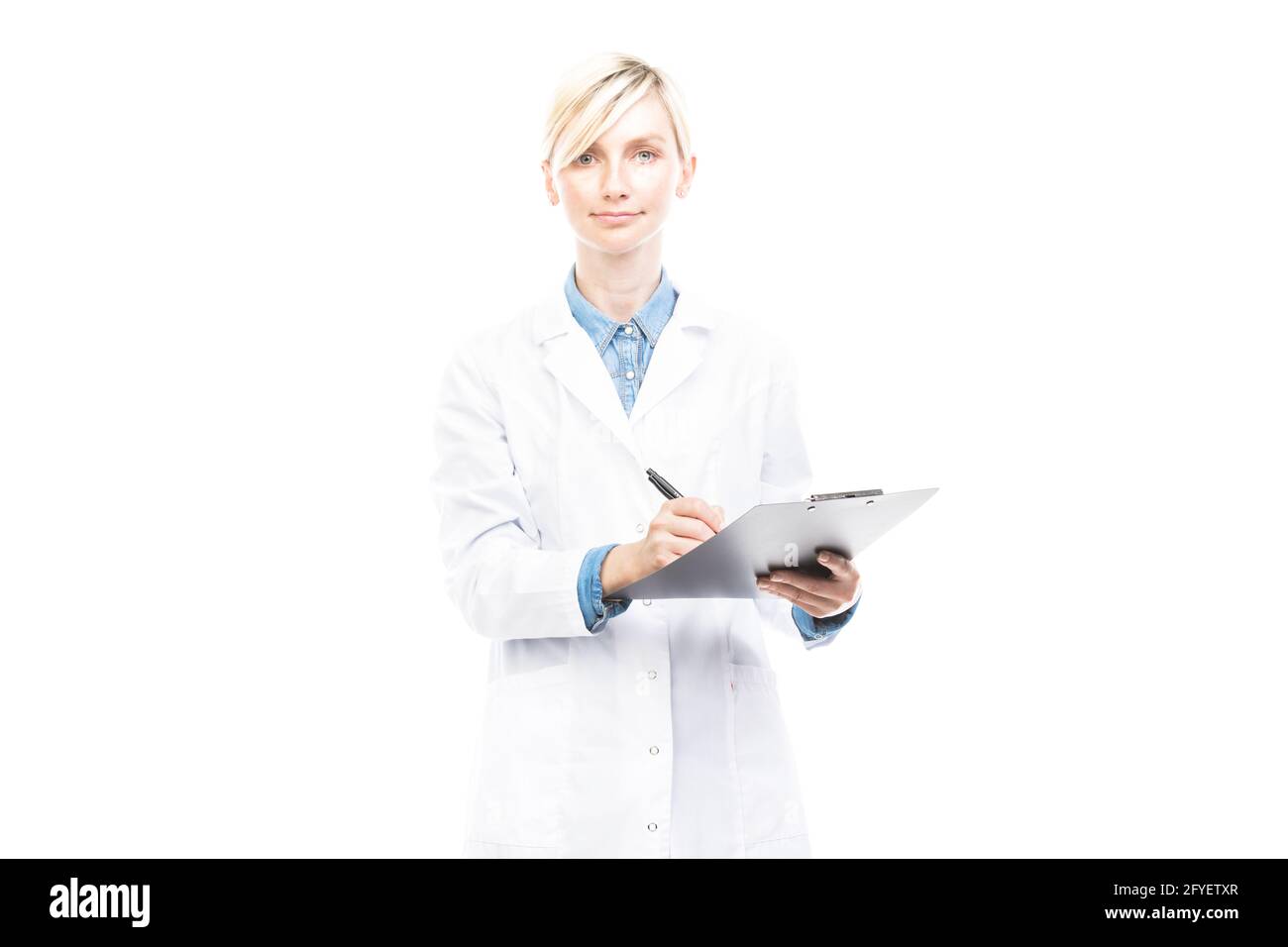 Portrait horizontal moyen de beau médecin caucasien portant un manteau blanc tenant le presse-papiers avec la carte médicale faisant des notes, fond blanc Banque D'Images