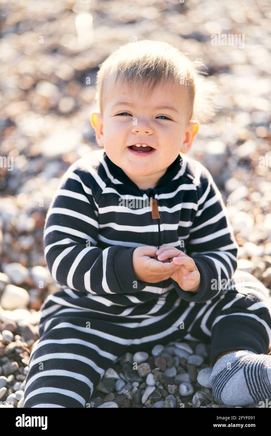 Un Petit Bebe Souriant Dans Une Combinaison Rayee Se Trouve Sur Une Plage De Galets Gros Plan Photo Stock Alamy