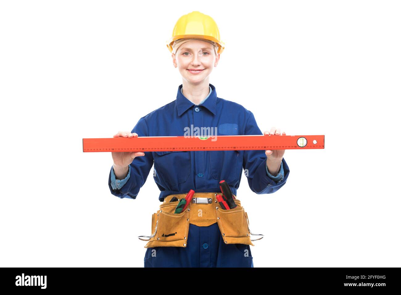 Portrait horizontal moyen d'une femme moderne de construction portant un uniforme bleu à l'aide d'un outil de niveau à bulle, fond blanc Banque D'Images