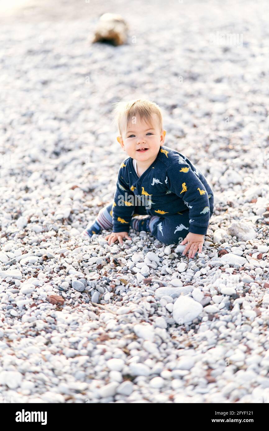 Un Petit Bebe Souriant Dans Une Combinaison Est Assis Sur Une Plage De Galets Gros Plan Photo Stock Alamy