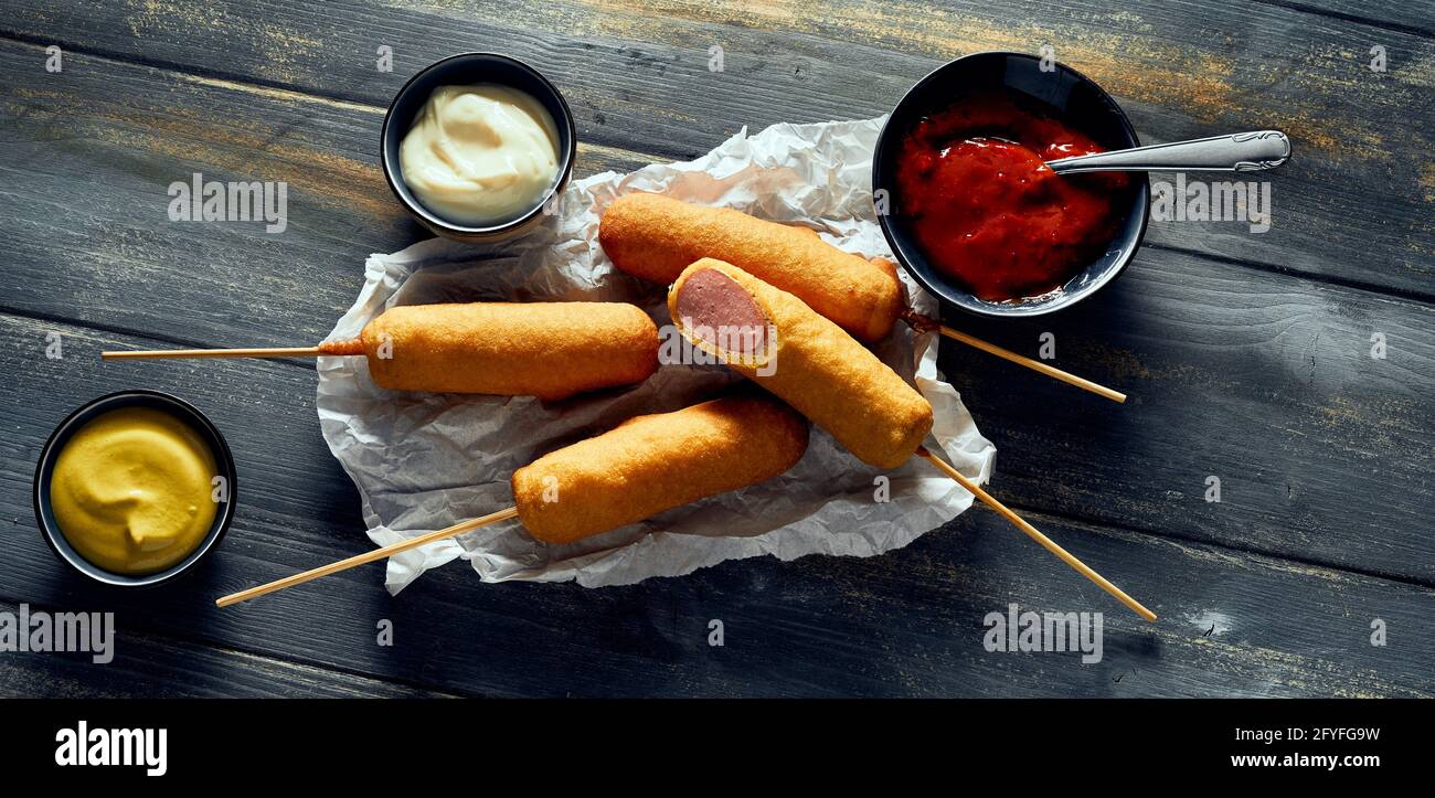 Vue de dessus délicieux chiens de maïs fraîchement frits servis sur des mouchoirs près de la crème sure de tomate et de la moutarde Banque D'Images