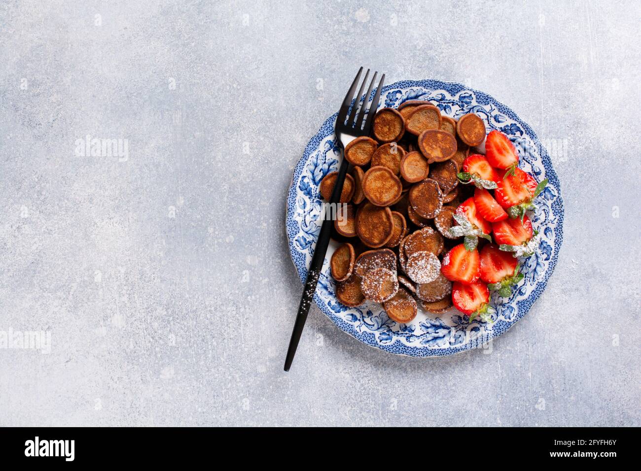 Mini céréales à crêpes au chocolat avec fraises pour le petit-déjeuner sur nappe en textile gris ancien. Petit déjeuner à la mode avec de minuscules crêpes. Vue de dessus Banque D'Images