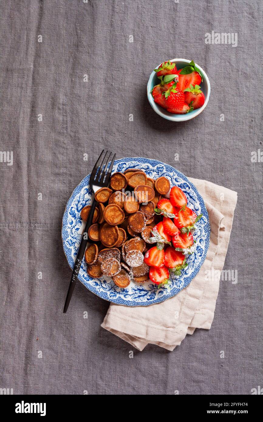 Mini céréales à crêpes au chocolat avec fraises pour le petit-déjeuner sur nappe en textile gris ancien. Petit déjeuner à la mode avec de minuscules crêpes. Vue de dessus Banque D'Images